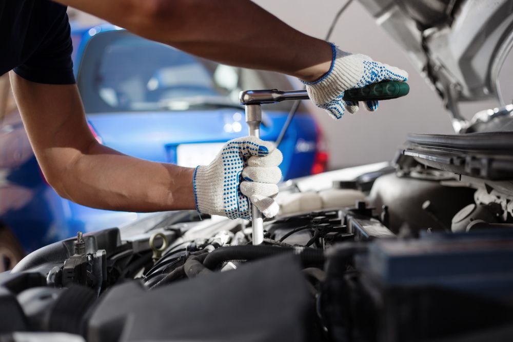 Mechanic using a wrench to perform auto repair on a vehicle's engine, emphasizing the importance of regular maintenance for car care.