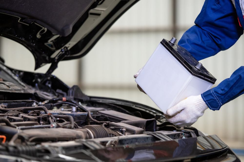 Automotive technician replacing a car battery in an engine bay, highlighting battery maintenance and repair services.