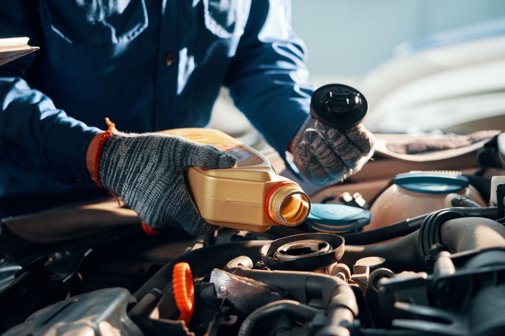 Mechanic pouring engine oil into a vehicle while holding an oil filter, emphasizing the importance of regular oil changes for vehicle maintenance.