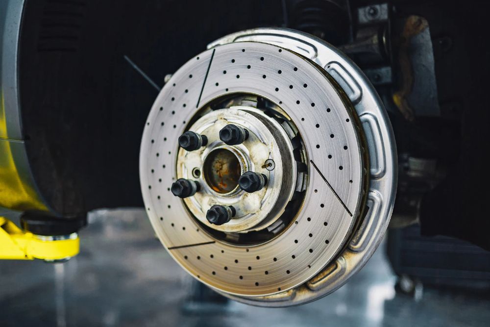 Close-up of a vehicle brake rotor and hub assembly, showcasing drilled holes for heat dissipation, relevant to automotive brake repair and maintenance.