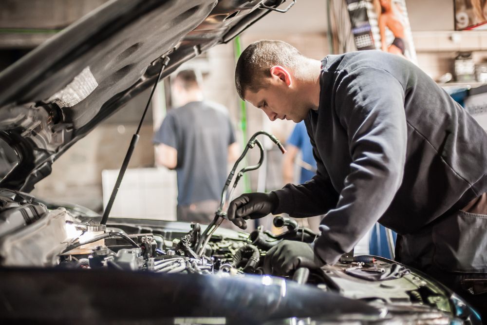 Mechanic working on a car engine in an auto repair shop, emphasizing general auto repair and vehicle maintenance.