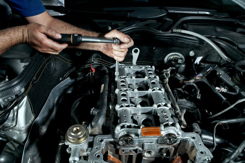 Mechanic using a wrench to repair an engine component under the hood, highlighting general auto repair and maintenance.